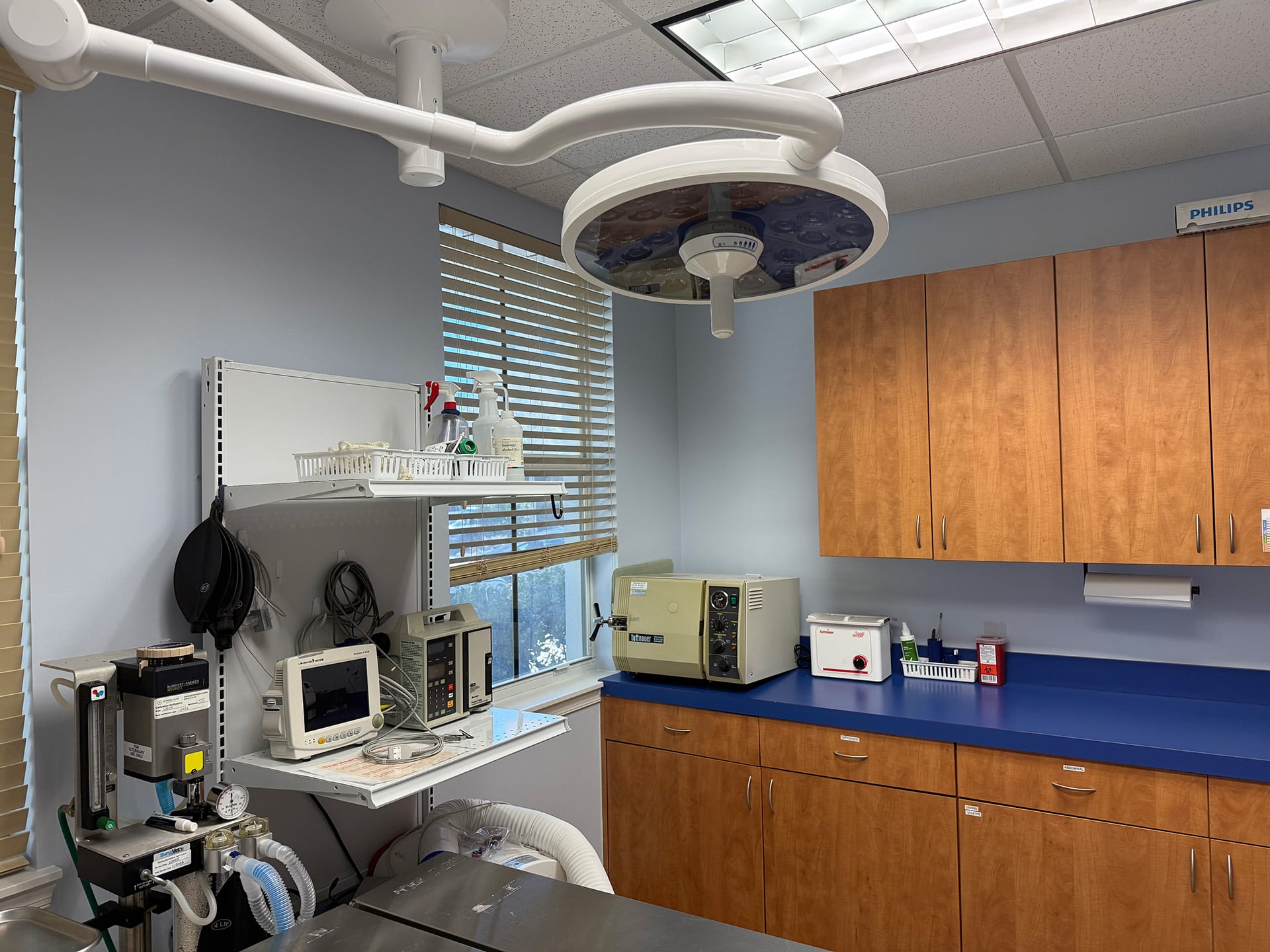 Medical equipment in a clinic, with monitors, a sterilizer, and wooden cabinets in a well-lit room.